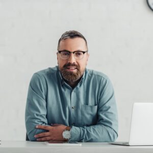 handsome businessman in shirt and glasses looking at camera in office