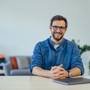 Confident man in casual attire smiling at camera in a contemporary office environment.